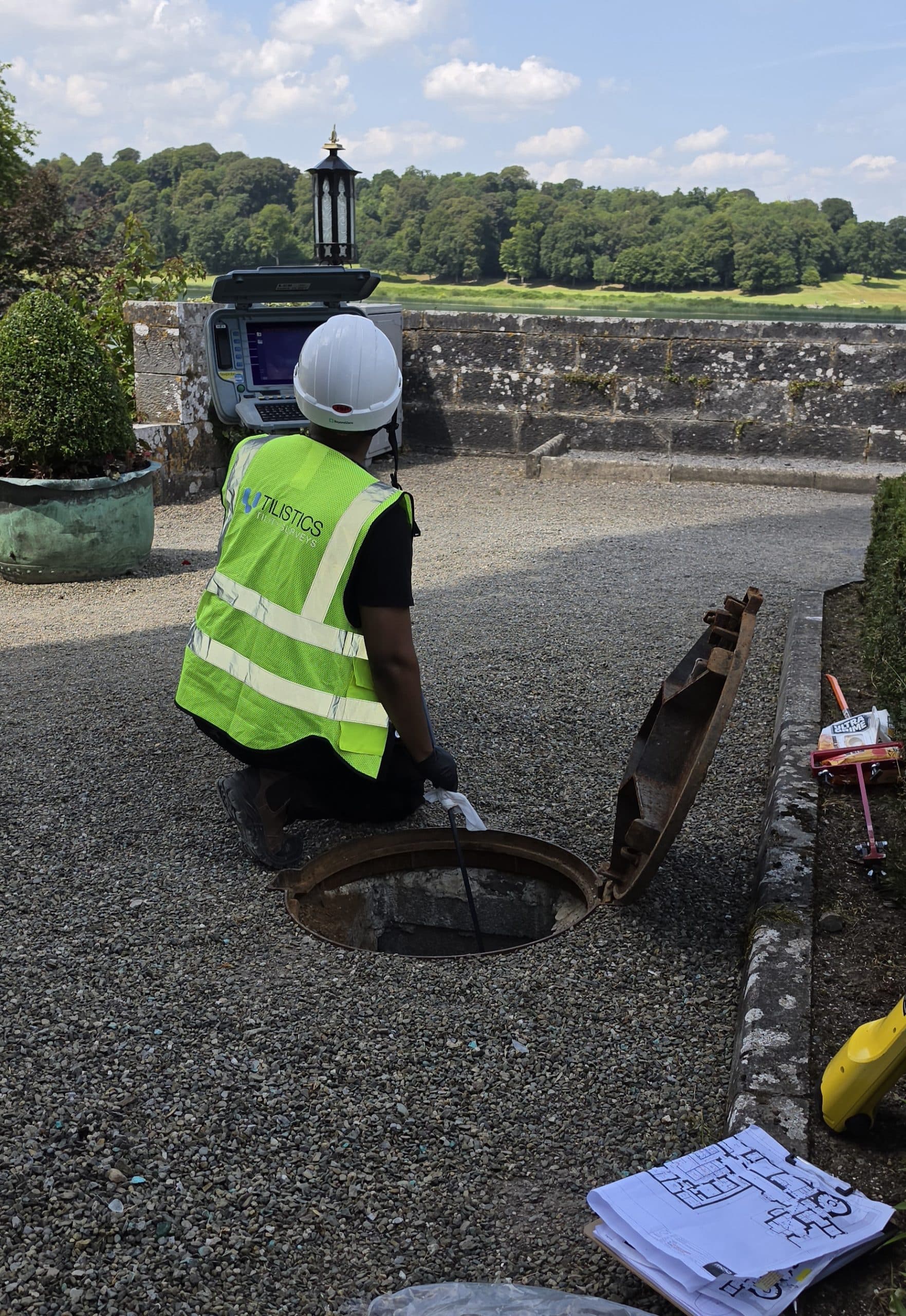 Utilistics technician using a CCTV inspection controller and push rod beside an open drainage chamber.